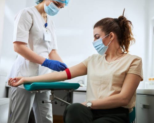Skilled focused young phlebotomy technician applying a tourniquet to a female patient arm for venipuncture